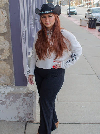 Model is wearing a wide leg black pant with a ribbed texture. Pants are stretchy and pull on. Pants worn with brown boots and a white sweater.