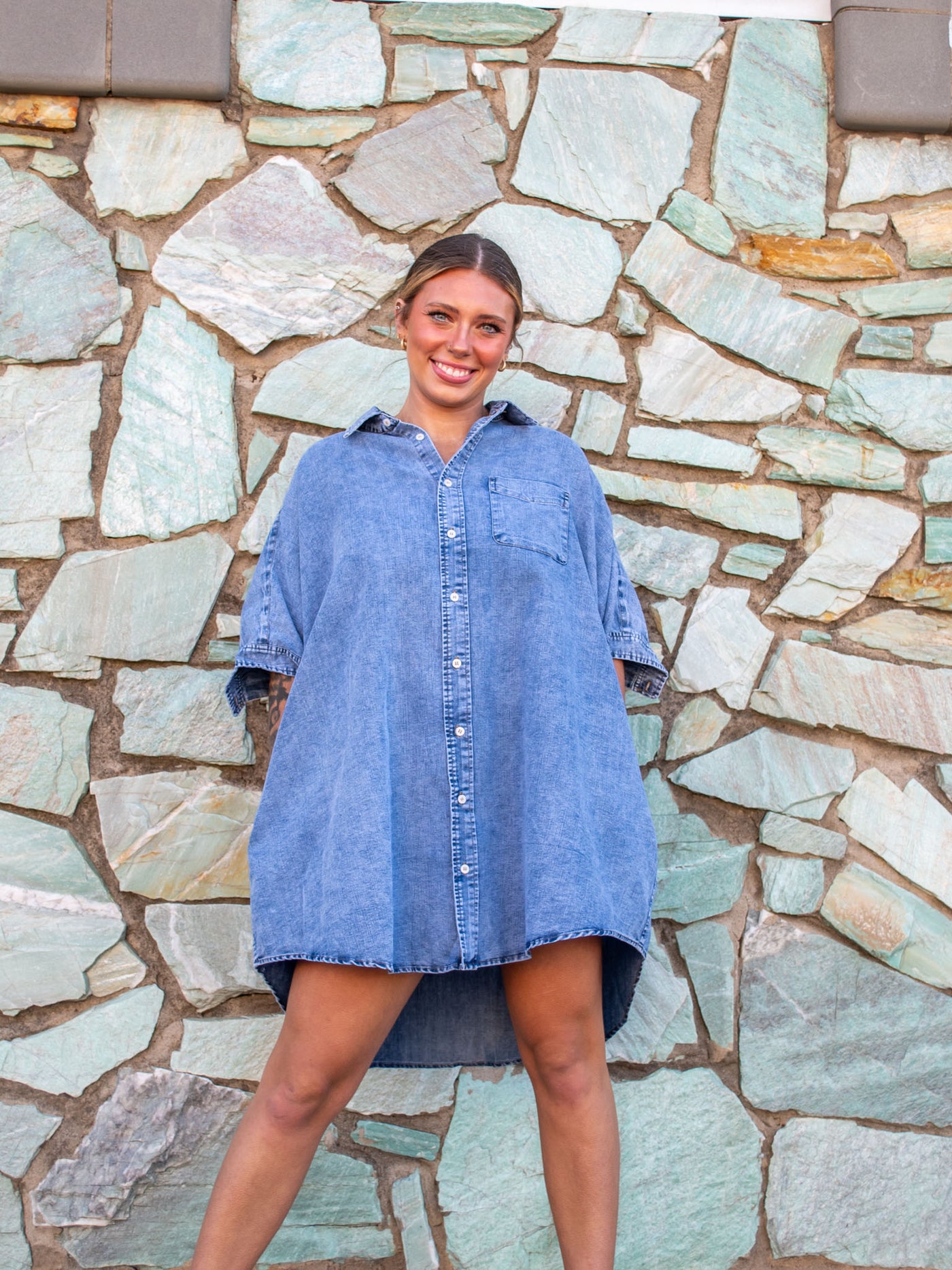 A model wearing a denim wash oversized fit, button up dress with a collar and chest pocket.