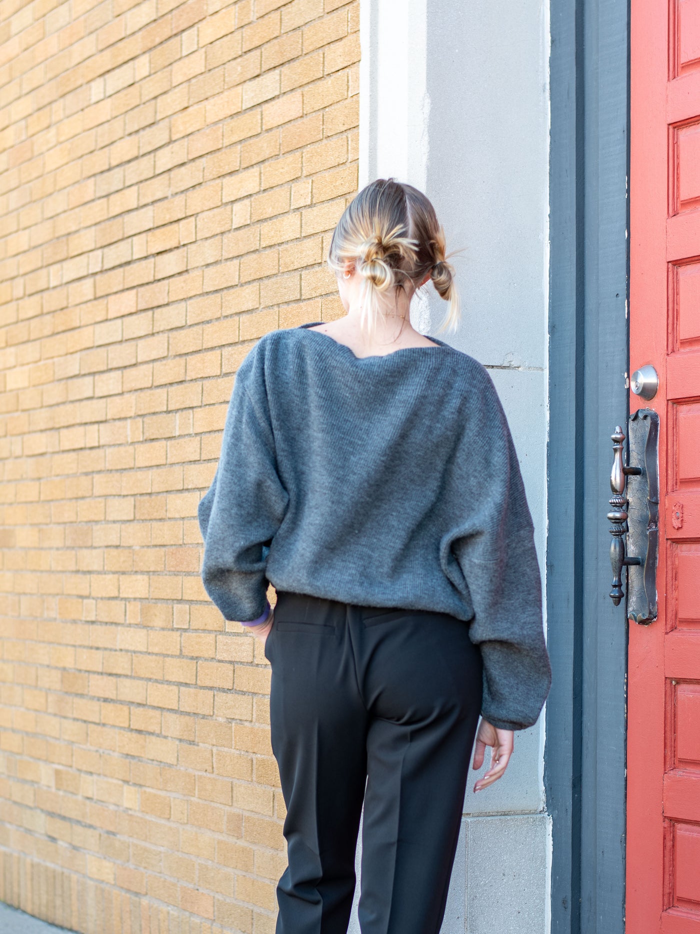 A model wearing a gray sweater with an adjustable waist. The model has it paired with black trousers.