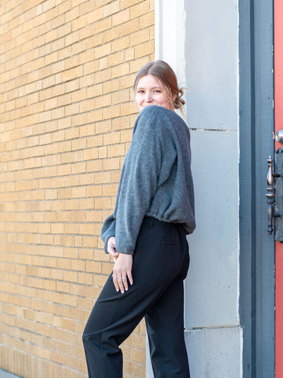 A model wearing a gray sweater with an adjustable waist. The model has it paired with black trousers.
