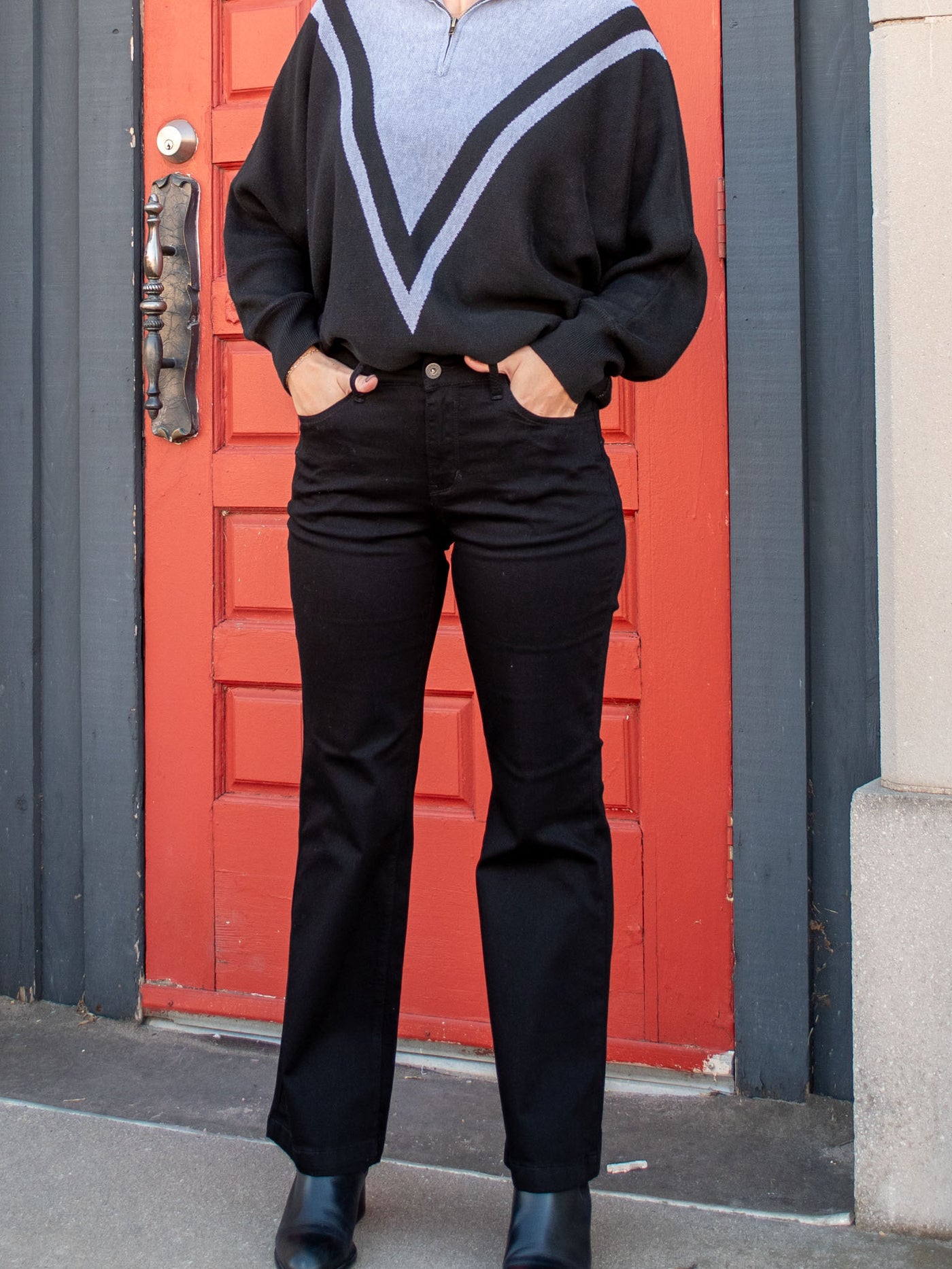 A model wearing a pair of black flare clean jeans. The model has it paired with a black and gray 1/4 zip sweater and black booties.