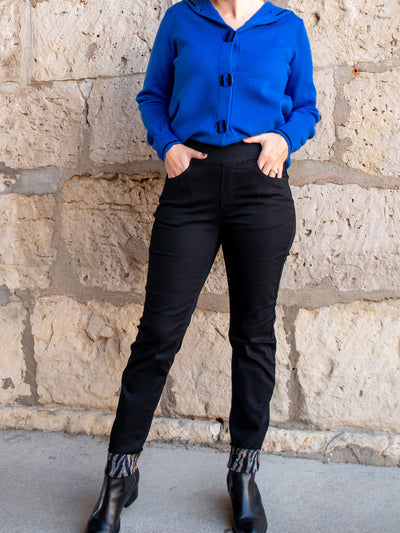 A model wearing a pair of black slim fit jeans with a black and zebra sparkle ankle cuff. The model has it paired with black booties and a blue sweater. 