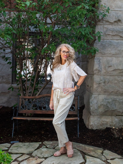 A model wearing a pair of tan drawstring waist denim joggers with an eyelet floral top. She has it paired with sandals.