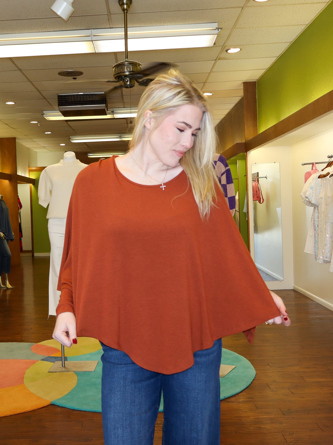 Model is wearing a rust colored reversible longsleeve with a built in shawl that can be reversible to however model wants it to lay. Long sleeve is paired with blue jeans.