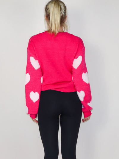 Model is wearing a dark hot pink knitted sweater with light pink hearts. Sweater is paired with black leggings. 