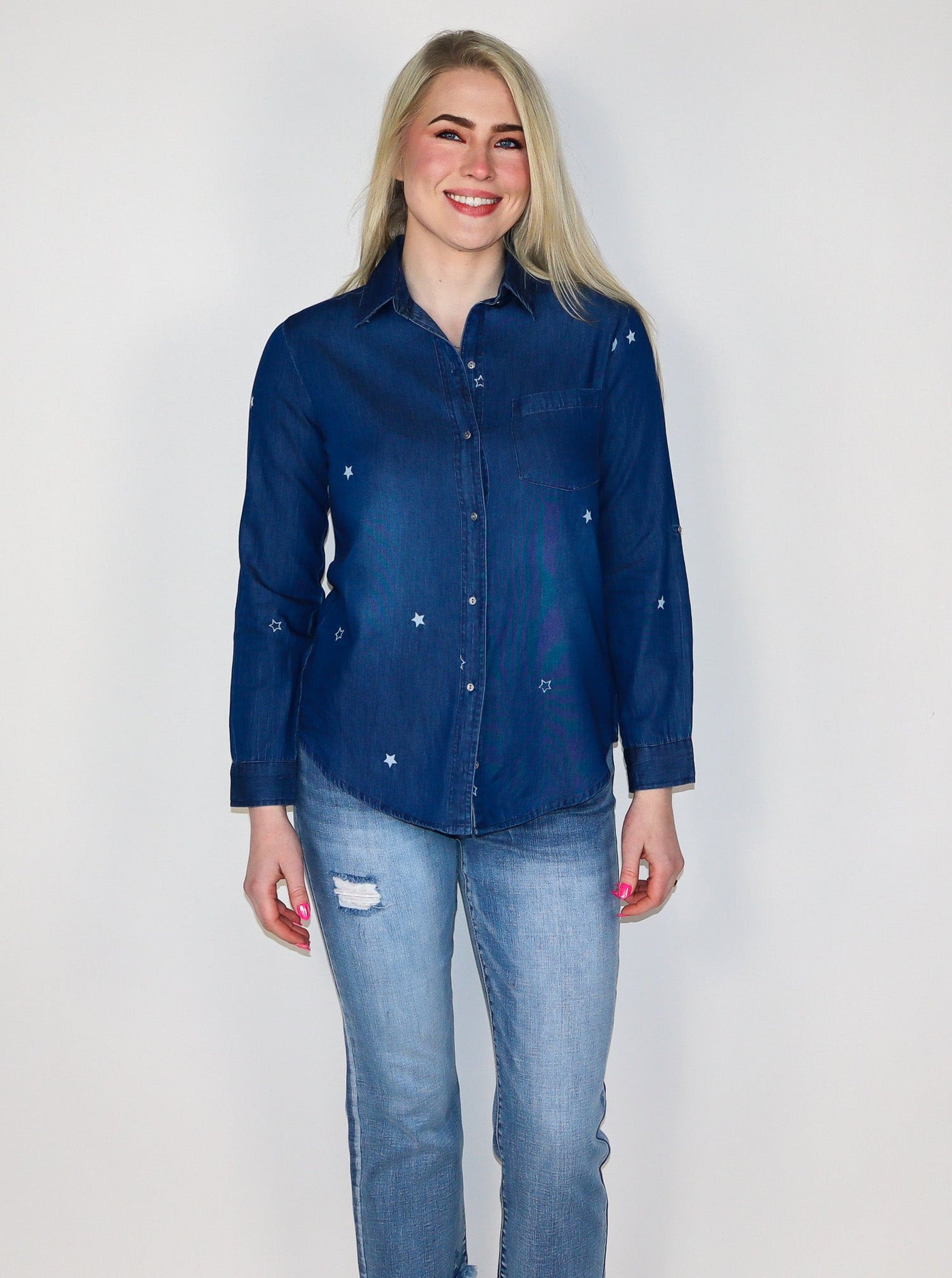 Model is wearing a dark blue wash denim button up with white stars all over. Top is worn with blue jeans. 