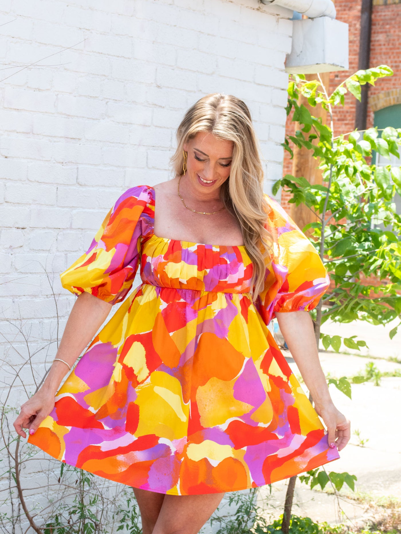 A model wearing a pink, orange, purple, and yellow empire waist mini dress with puff sleeves. She has paired it with brown platform sandals.