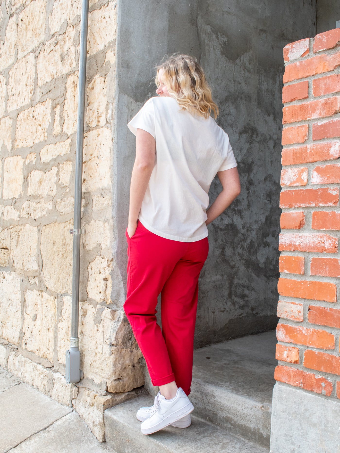 A model wearing a pair of red denim joggers with a drawstring waist. She has it on with a white crewneck short sleeve tee and white sneakers.