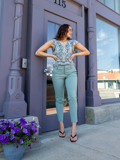 A model wearing a sea green trouser with a sea green and white blouse and black sandal paired with them.