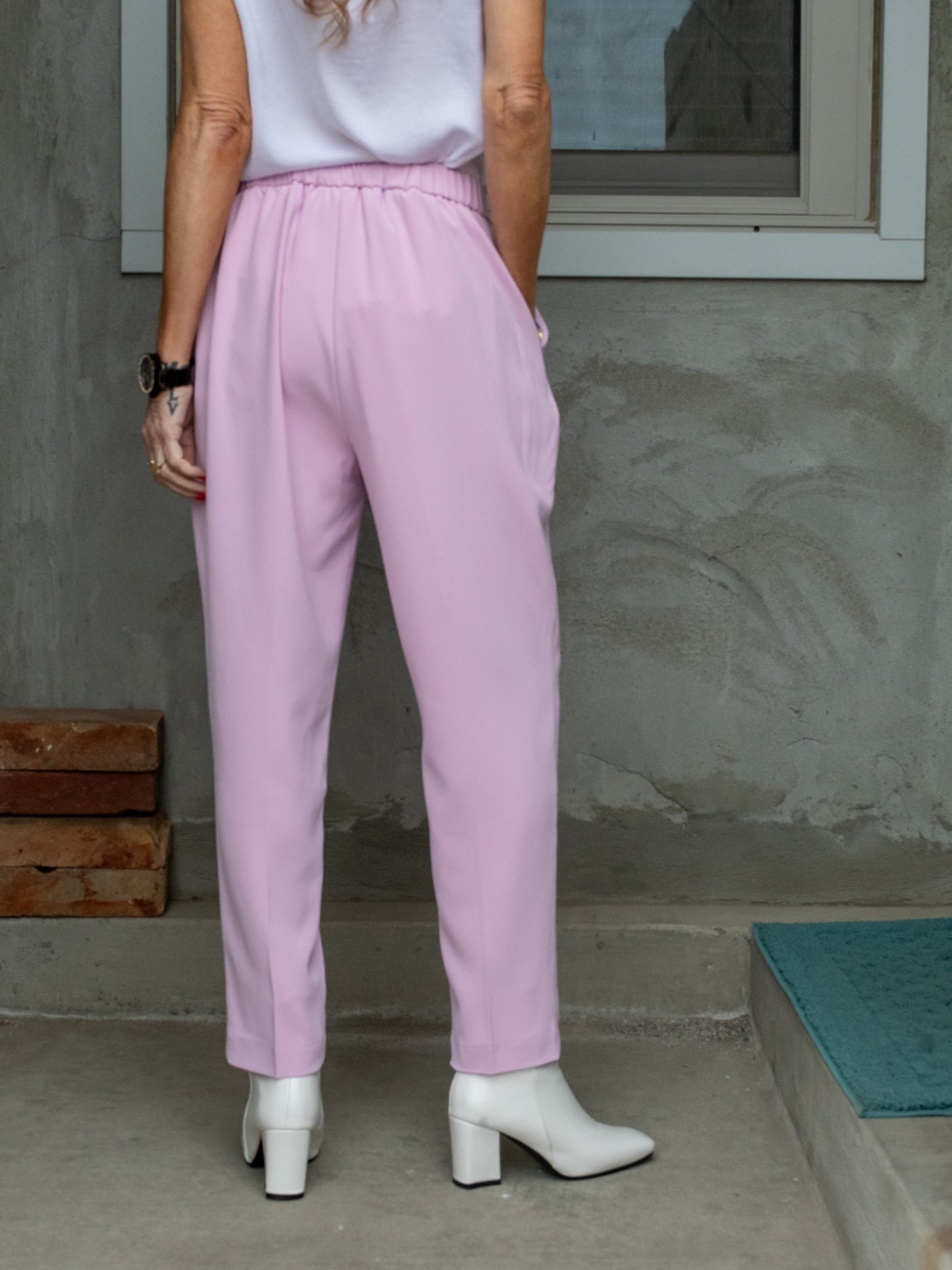 A model wearing lilac purple fitted pull on style pants with a matching blazer and v neck white top.