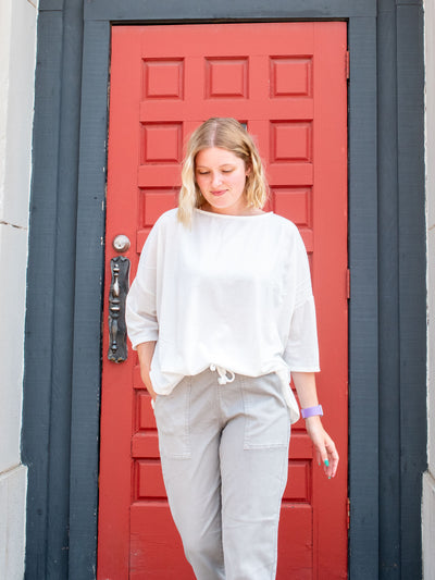 A model wearing an oversized drop sleeve ivory top. She has it paired with gray joggers.