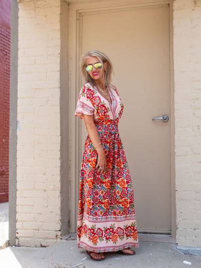A model wearing a red floral maxi dress. She has it paired with a pair of brown sandals.