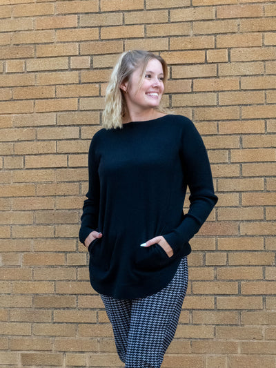 A model wearing a black knit sweater with a silver sleeve lace-up detail. The model has it paired with a pair of houndstooth pants.