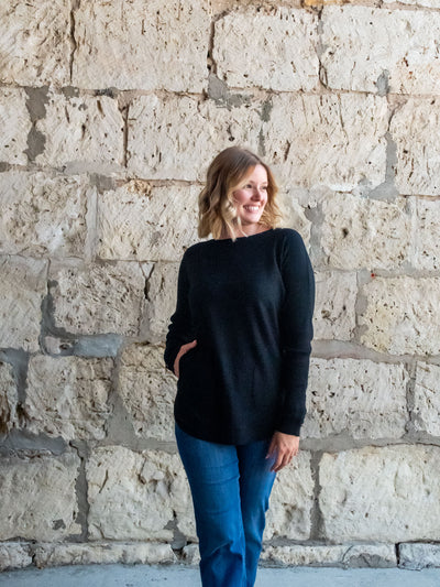 A model wearing a black sweater with a lace-up sleeve detail. The model has it paired with a medium wash straight leg jean.