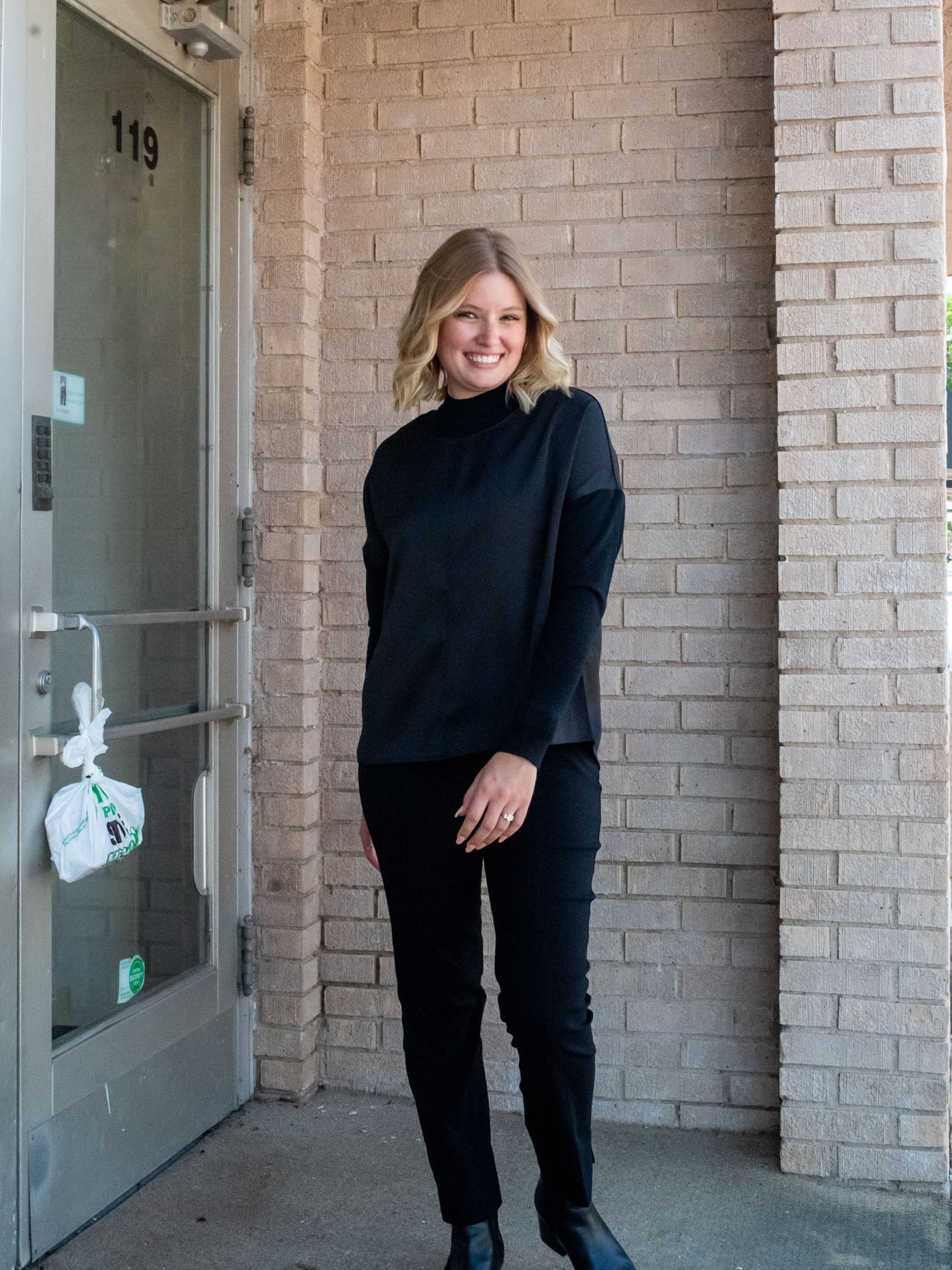 A model wearing a black top with knit sleeves. She has it paired with black pants and black booties.
