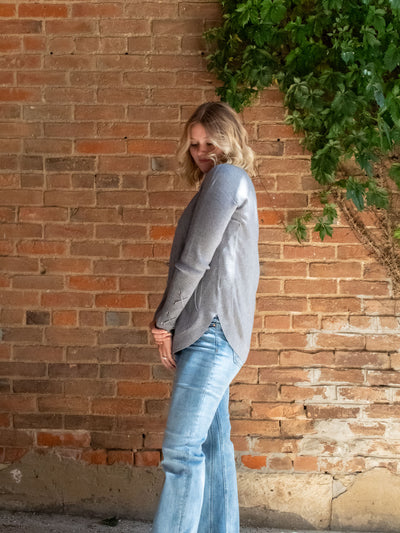 A model wearing a gray sweater with a lace-up sleeve detail. The model has it paired with a light wash straight leg jean.