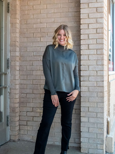 A model wearing an olive green top with knit sleeves. She has it paired with black pants.