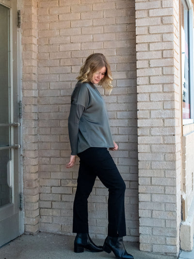 A model wearing an olive green top with knit sleeves. She has it paired with black pants and black booties.