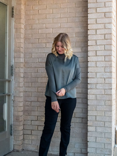 A model wearing an olive green top with knit sleeves. She has it paired with black pants.