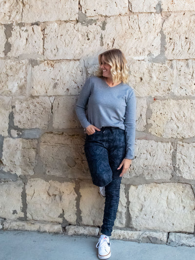 A model wearing a pair of navy, printed pants with a crinkle fabric. The model has them paired with a gray v-neck top and white sneakers.