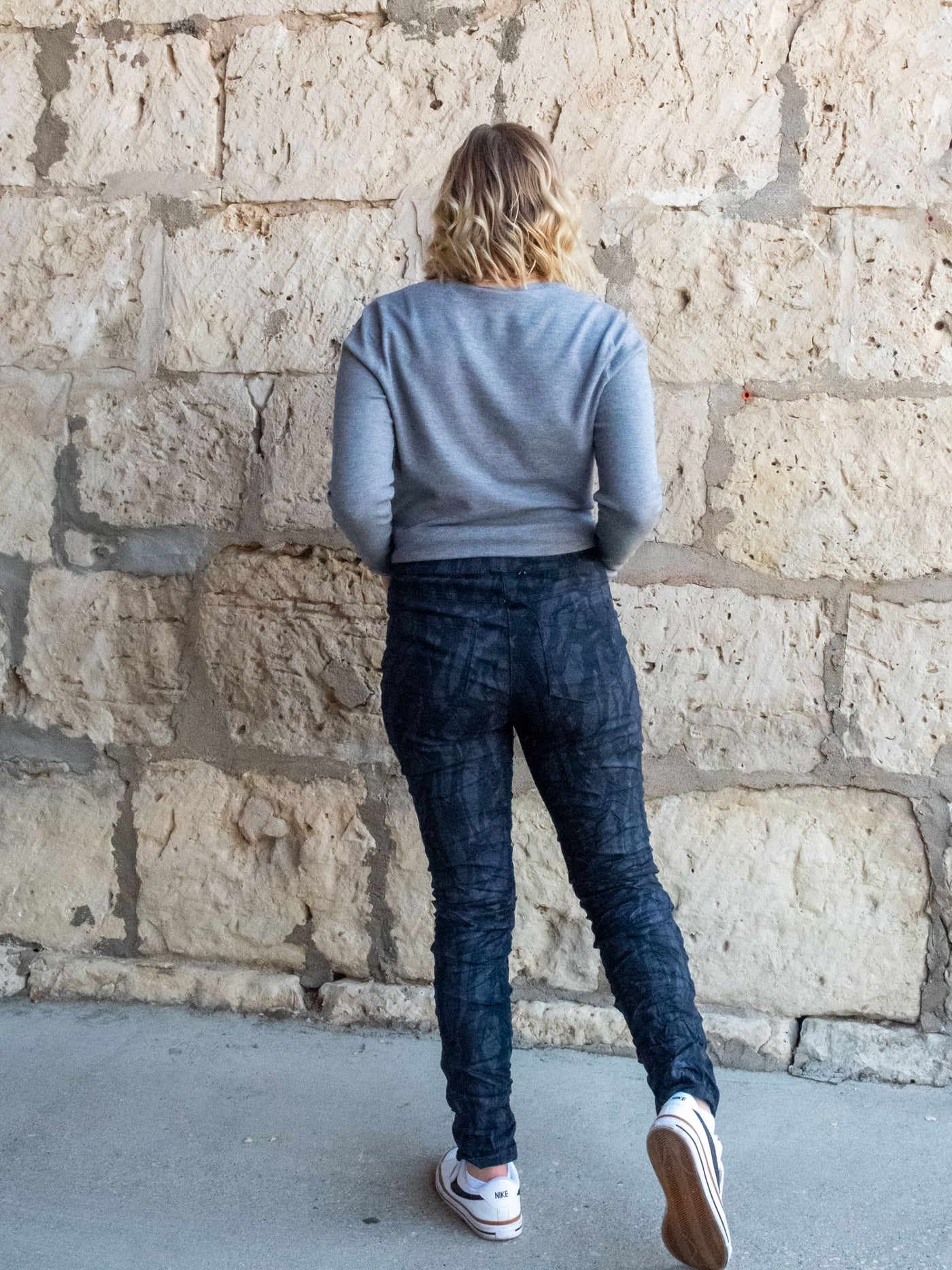 A model wearing a pair of navy, printed pants with a crinkle fabric. The model has them paired with a gray v-neck top and white sneakers.