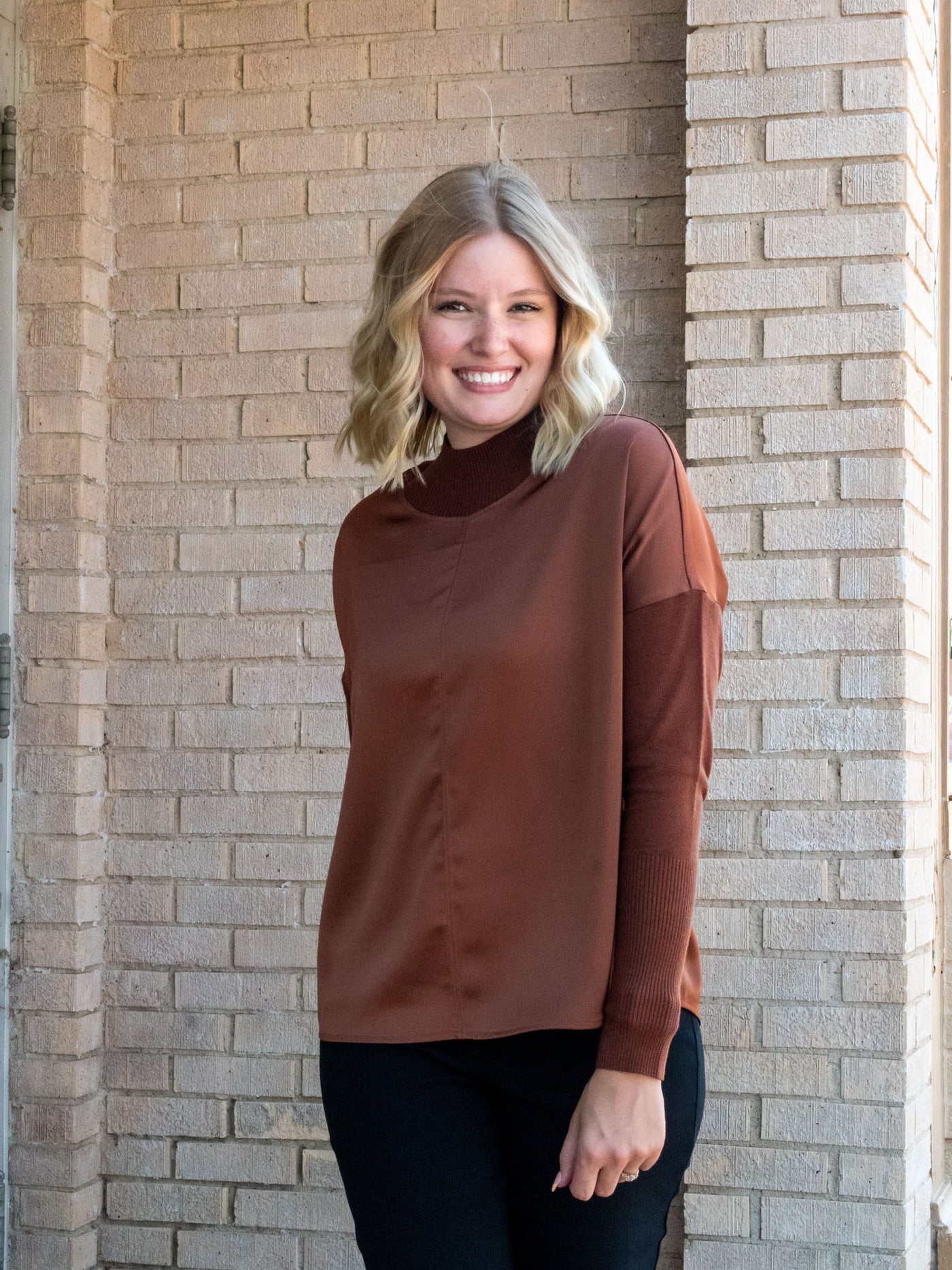 A model wearing a rust brown top with knit sleeves. She has it paired with black pants.