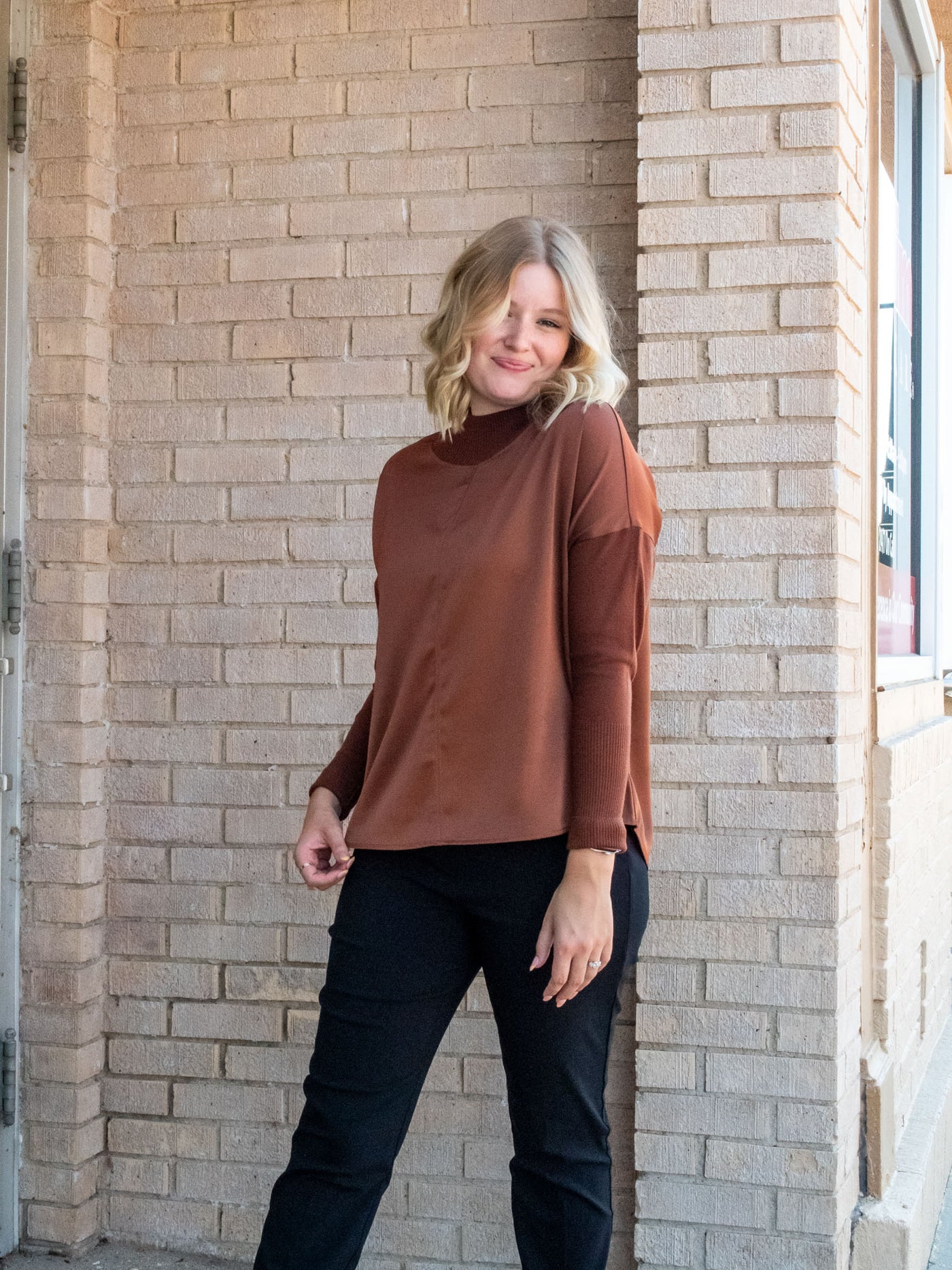 A model wearing a rust brown top with knit sleeves. She has it paired with black pants.