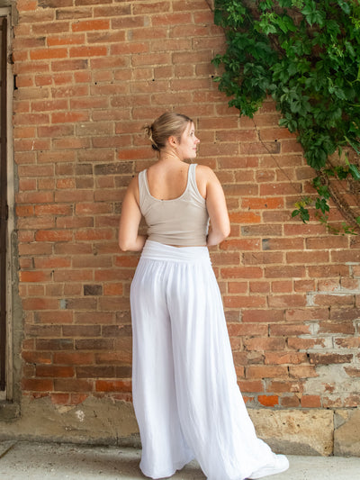 A model wearing a pair of white, flowy silk pants. The model paired them with a beige tank top.