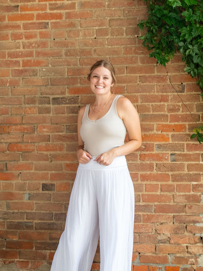 A model wearing a cream ribbed cropped tank top. She has paired it with a pair of flowy silk pants.