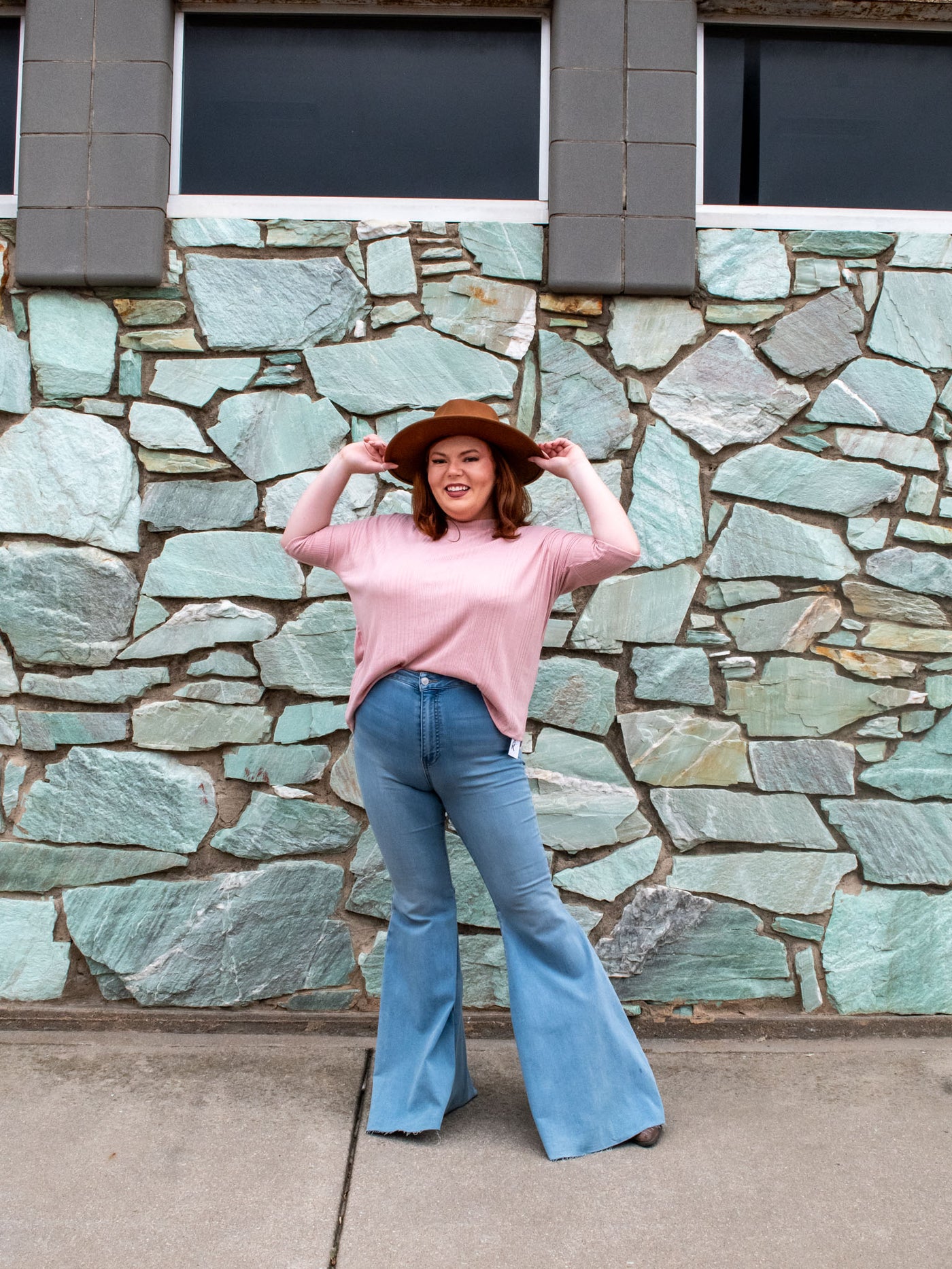 A model wearing a pink ribbed top with a 3/4 length sleeve. The model has it styled with a pair of ultra flare, high waisted jeans and a primmed hat.