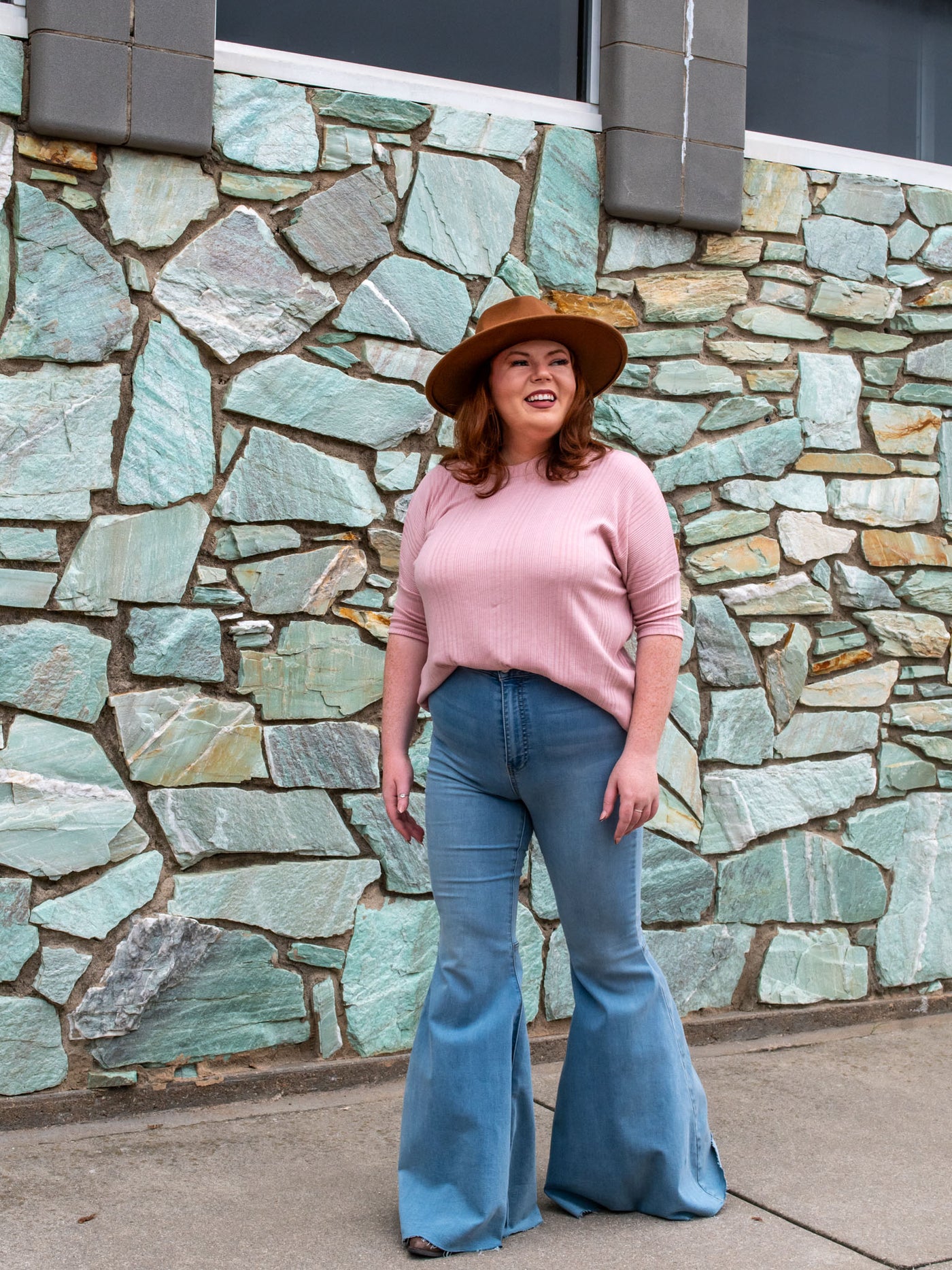 A model wearing a pink ribbed top with a 3/4 length sleeve. The model has it styled with a pair of ultra flare, high waisted jeans and a primmed hat.