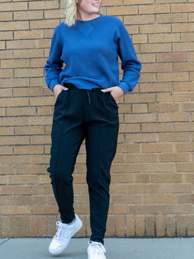 A model wearing a pair of black joggers with a seam detail. The model has it paired with a blue waffle knit top and white sneakers.