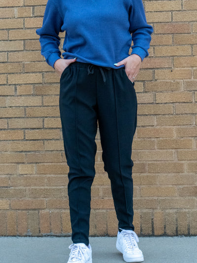 A model wearing a pair of black joggers with a seam detail. The model has it paired with a blue waffle knit top and white sneakers.