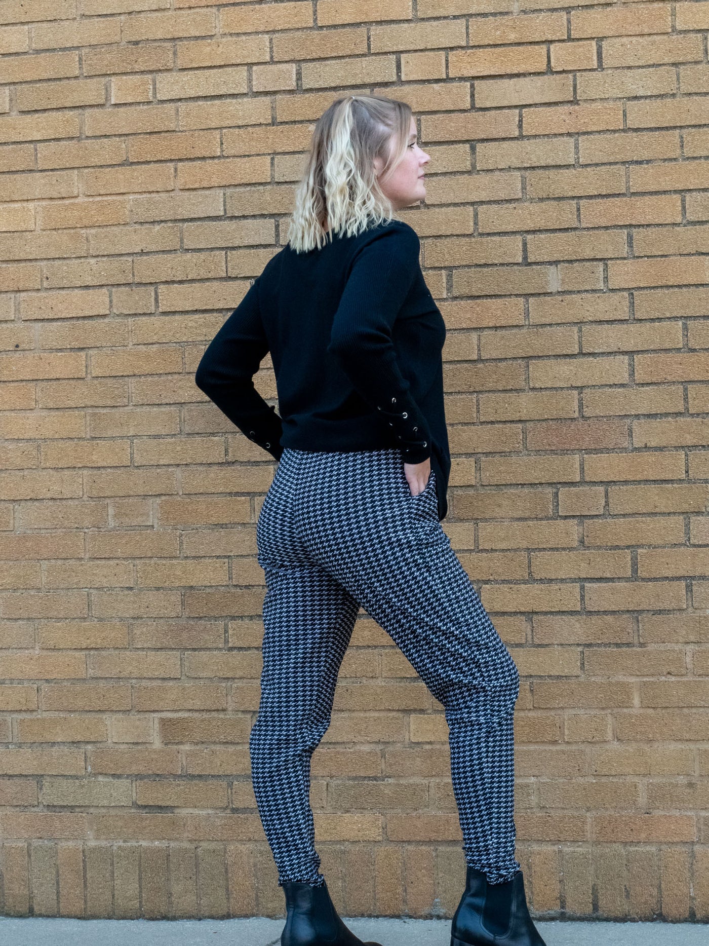 A model wearing a pair of black and white houndstooth joggers. The model has them paired with a black sweater and black booties.
