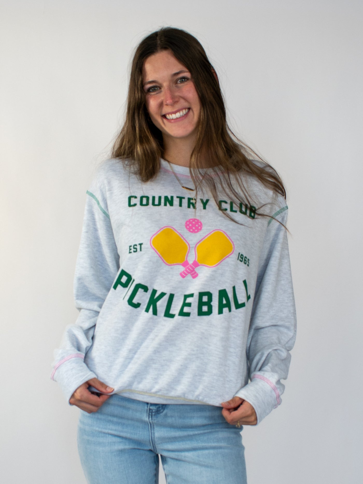 Model wearing grey heathered crewneck with green lettering that says country club and pickle ball. There is also a yellow and pink pickleball graphic!