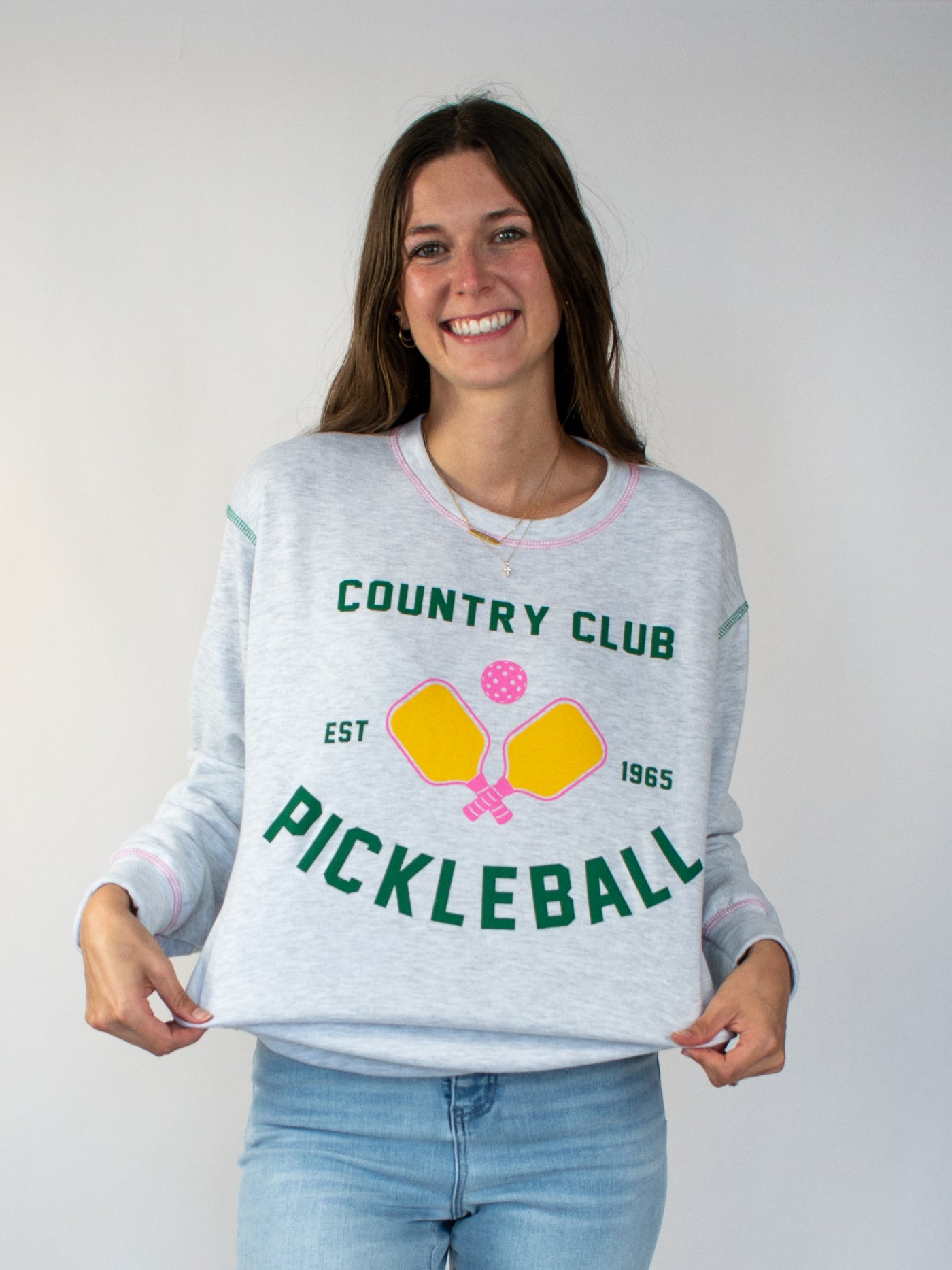 Model wearing grey heathered crewneck with green lettering that says country club and pickle ball. There is also a yellow and pink pickle ball graphic!