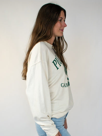 Model wearing a cream crewneck sweatshirt with green lettering that says Pickle Ball and Game, Set, Match with a pickle ball paddle graphic. 