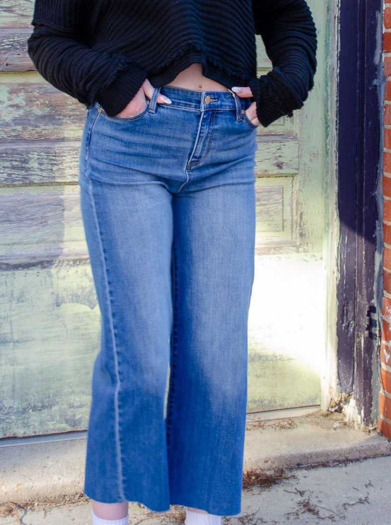 Model wearing The Essential Blue Jeans with a black cropped sweater and white tennis shoes.