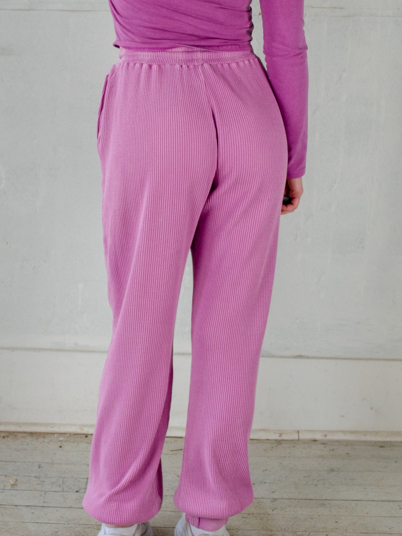 Model is wearing ribbed purple sweatpants with a purple cropped half zip.