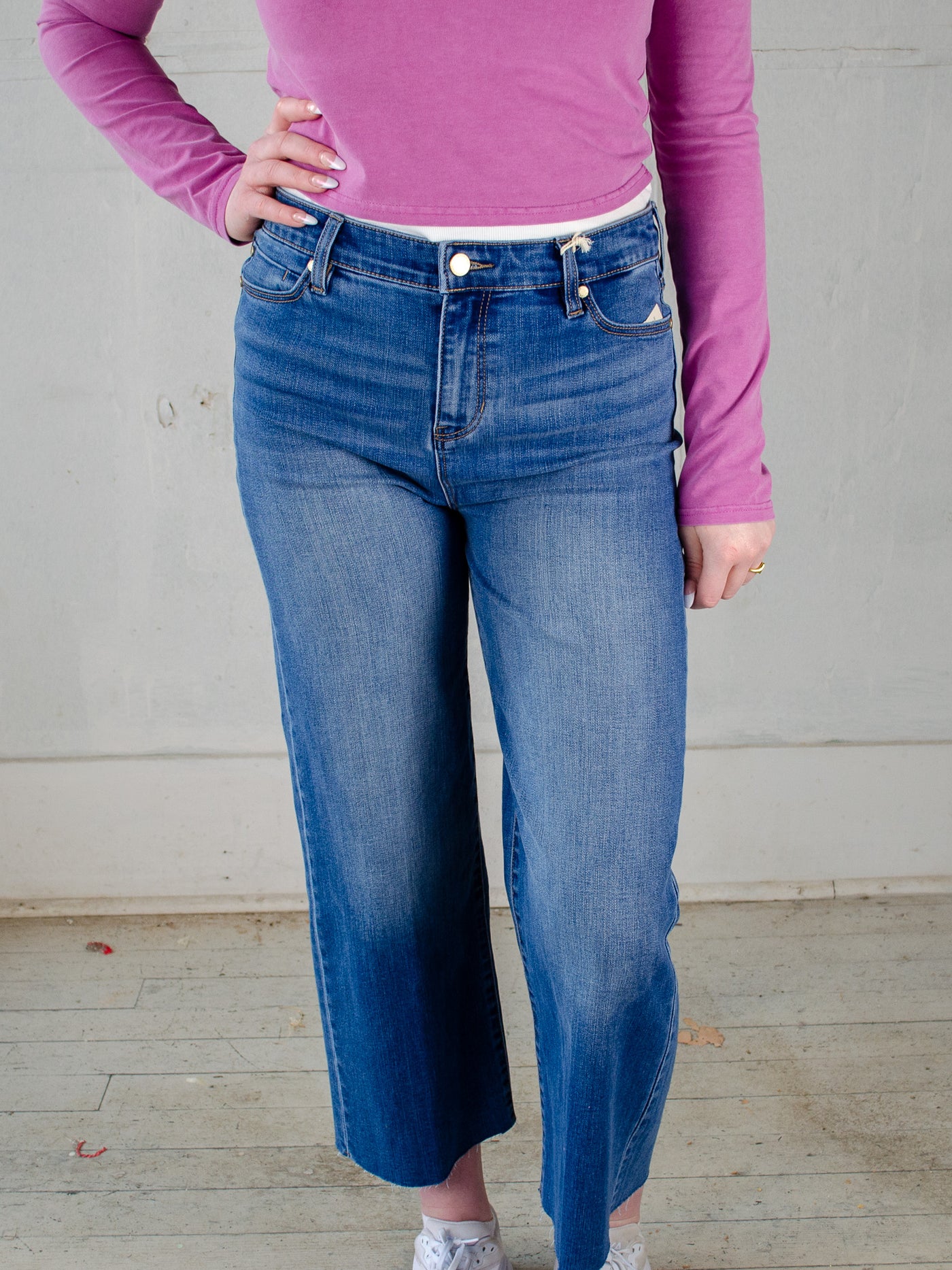 Model wearing The Essential Blue Jeans with a purple cropped quarter zip and white tennis shoes.