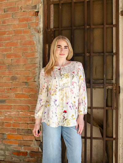 Model is wearing a long sleeve floral blouse with puff sleeves and lace detail on the chest. Blouse is worn with blue jeans.