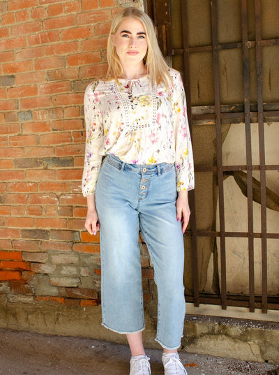 Model is wearing a high waisted light wash button up denim jean with frayed hemming at the ankles. Jeans are worn with a floral blouse. 