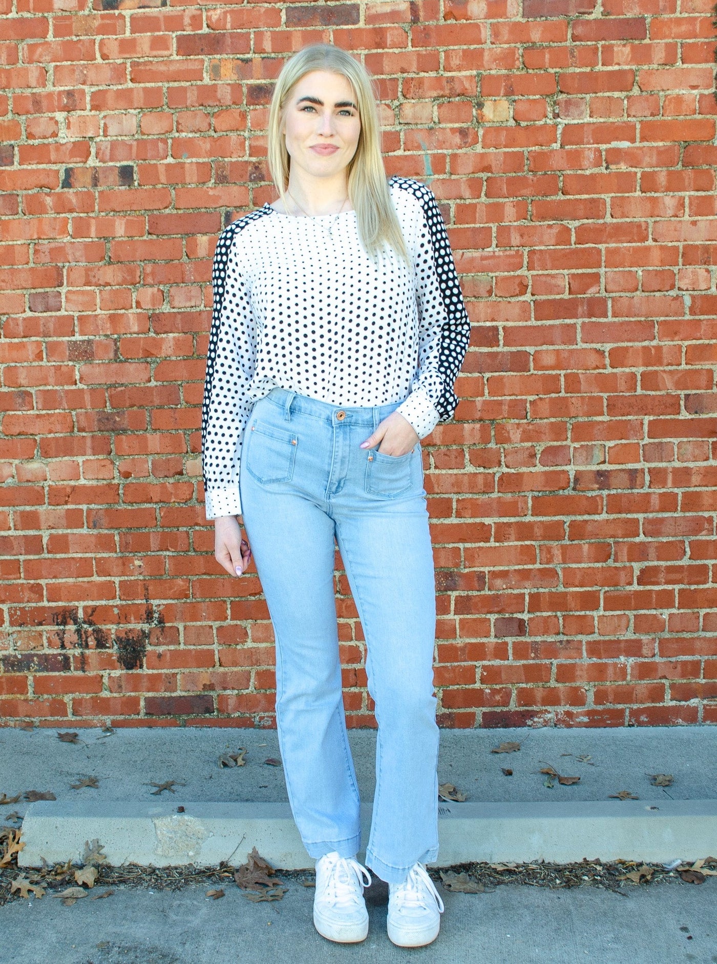 Model is wearing high rise light wash denim jeans with stitched pocket squares on the hips. jeans are worn with a polka dot blouse. 