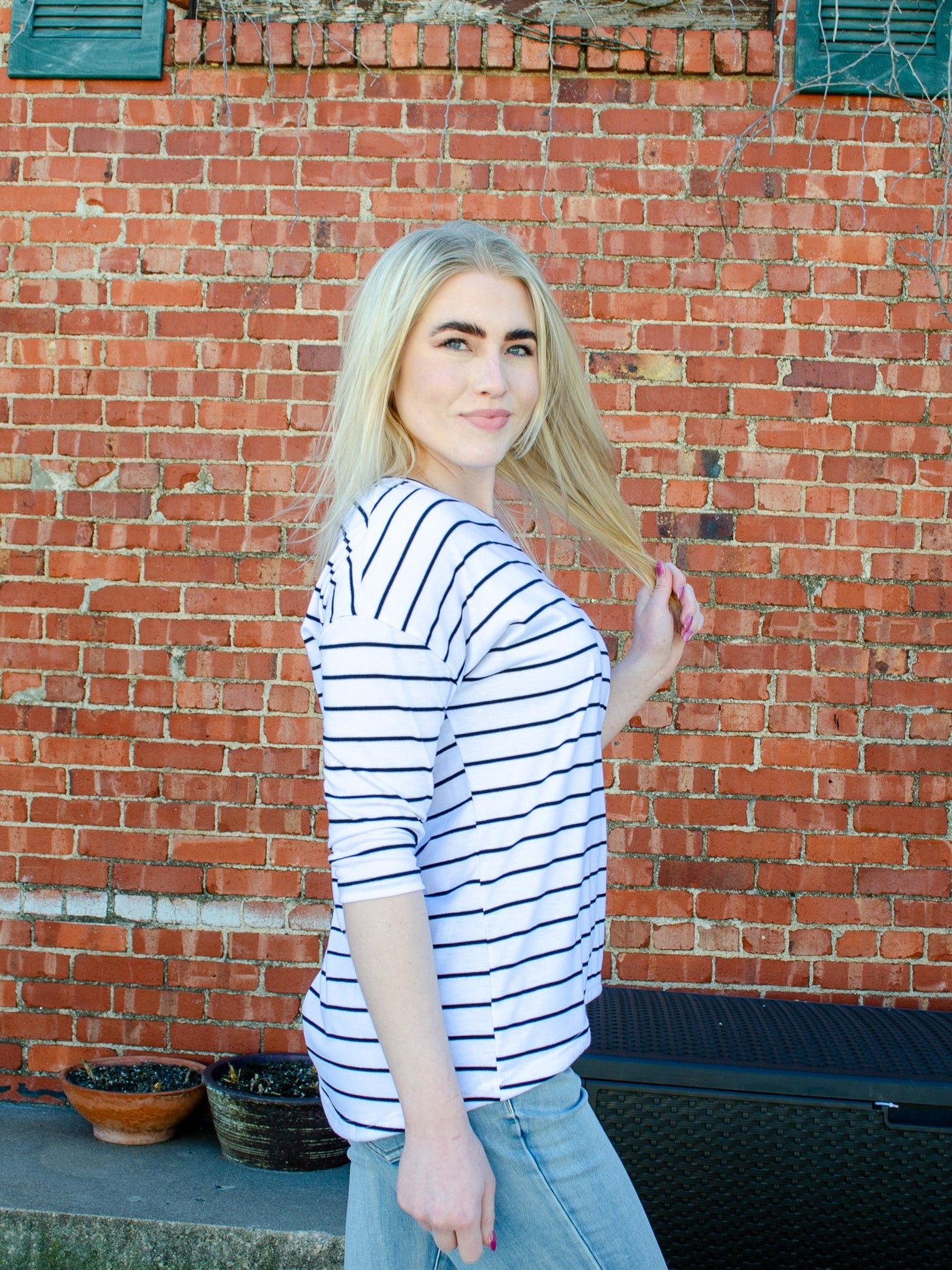Model is wearing a black and white horizontal striped 3/4th sleeve blouse. Blouse is worn with blue jeans. 