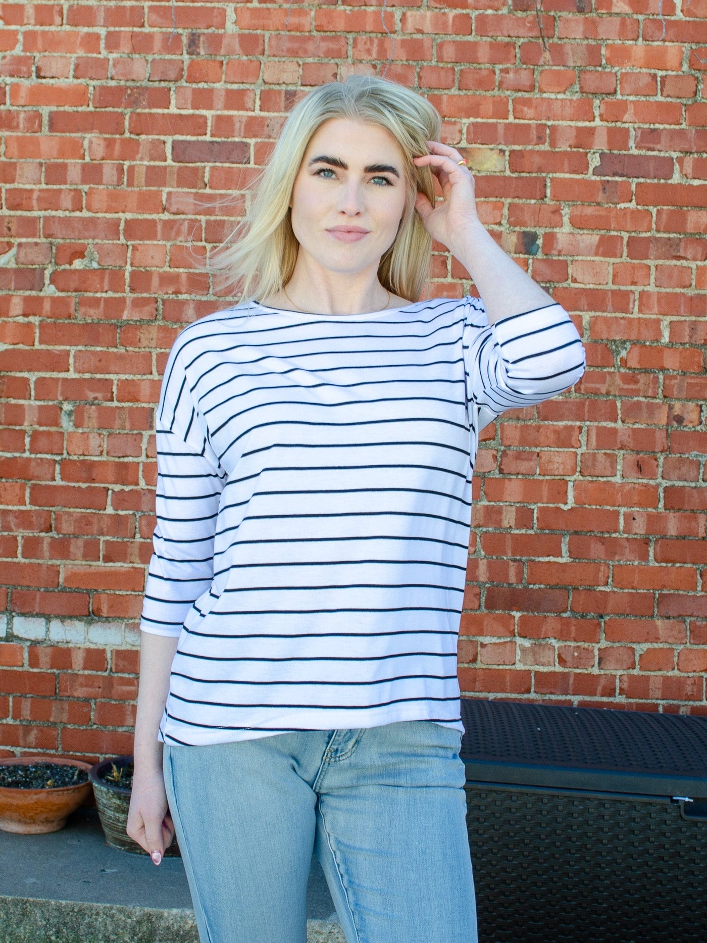 Model is wearing a black and white horizontal striped 3/4th sleeve blouse. Blouse is worn with blue jeans. 