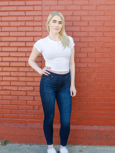 Model is wearing a dark wash skinny jean with a glide on feature that creates a easy glide on fit. Jeans are paired with a white tee