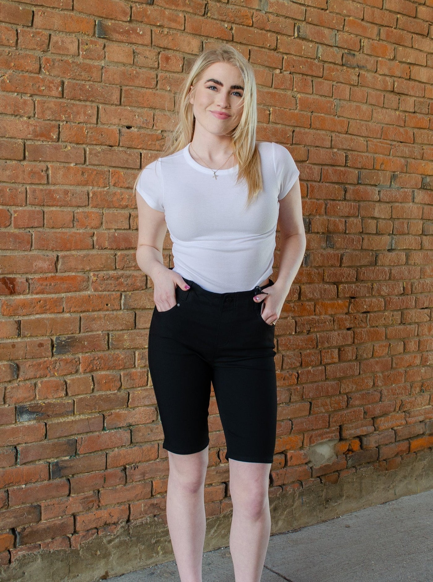 Model is wearing black thigh length denim shorts paired with a white t-shirt. 