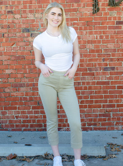 Model is wearing a light army green colored pull on skinny jean that is paired with a white t shirt. 