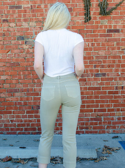 Model is wearing a light army green colored pull on skinny jean that is paired with a white t shirt. 