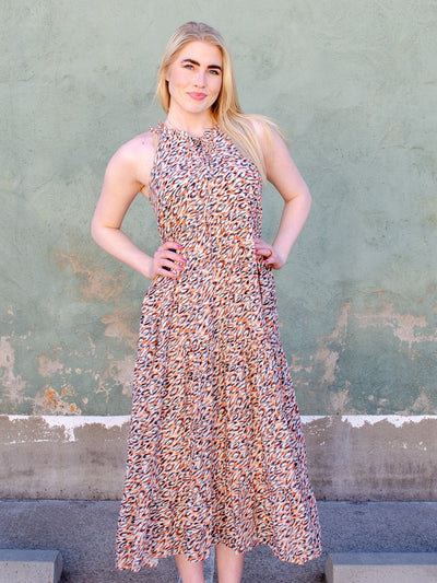 Model is wearing a multi colored long flowy dress with a mock neck-line. Dress is sleeveless and has a leopard print style of print. 